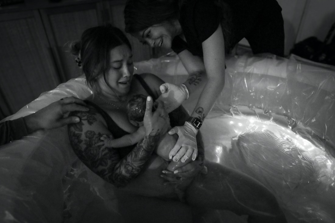 A mother holding her newborn in the first moments after birth, captured by a birth photographer